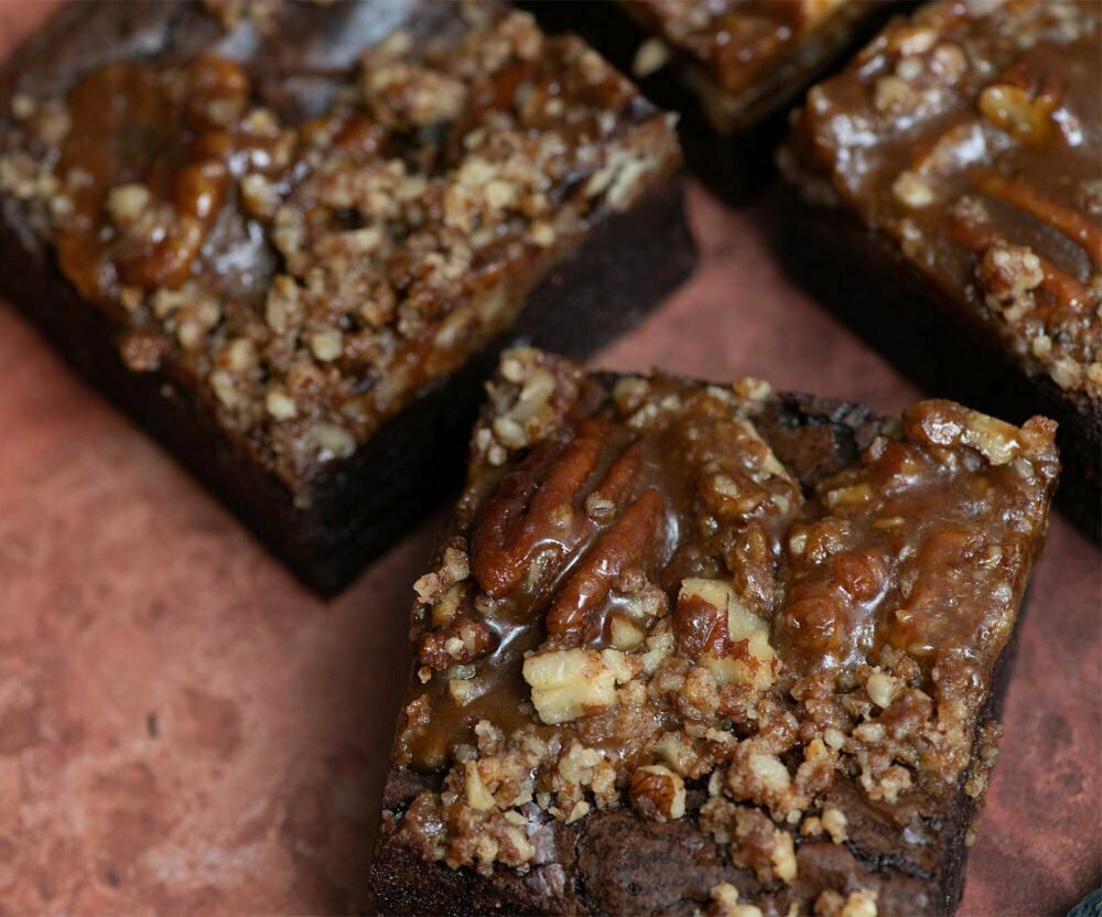 3 salted caramel and pecan brownies on a brown marbled background.