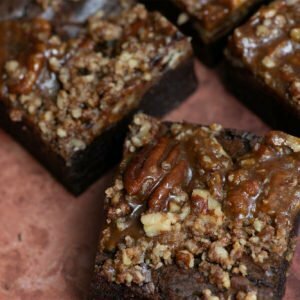 An image of Brownie and The Bean's salted caramel and pecan brownies. There are 3 brownies in the image. The brownies are laid on a brown marbled background.