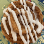 Cinnamon Roll on a heavily patterned plate with drizzled cream cheese icing