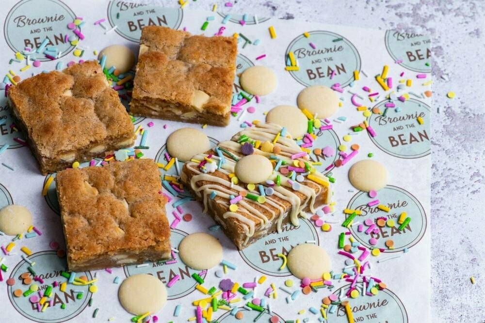 White Chocolate Funfetti Blondies with sprinkles and white chocolate buttons on branded greaseproof paper.