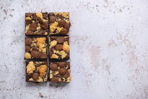 Billionaire Shortbread Brownie on a white marbled background. There are 6 brownies and there are chunks of shortbread scattered across the top of them.