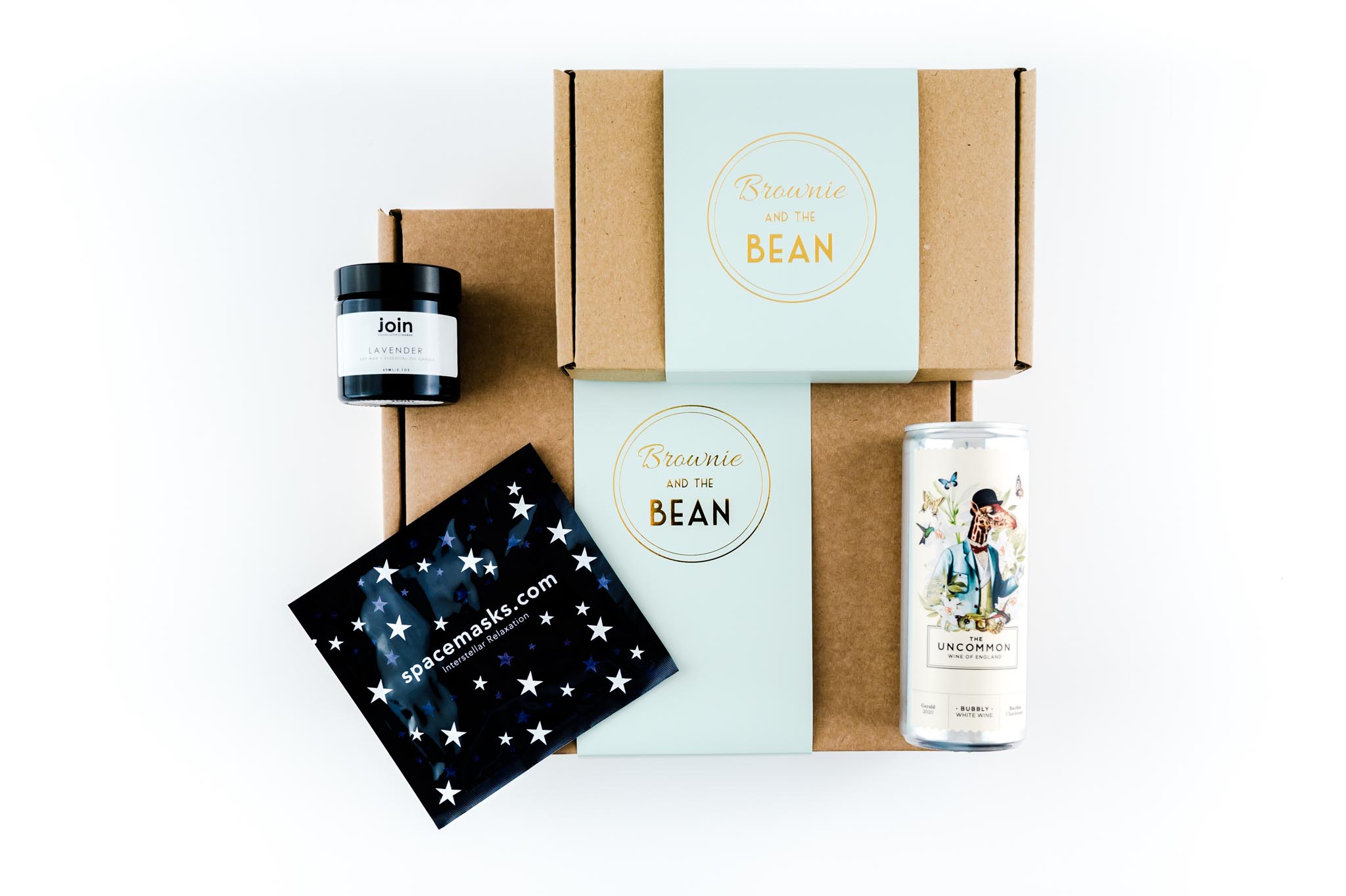 A corporate gifting bundle is in a flat lay position on a white background. There is Brownie and the Bean branded boxes, sparkling wine, a Spacemask and candle.