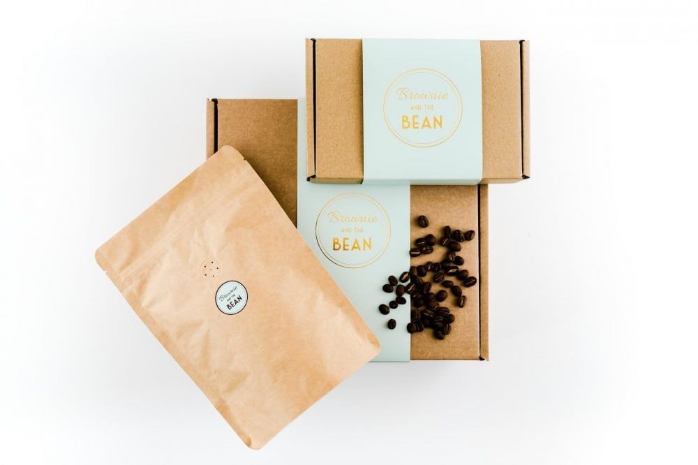 Brownie and The Bean's coffee and brownie gift set. A small branded gift box and a large packet of Butterworth & Son's coffee is balanced on top of a large branded gift box. There are loose coffee beans sprinkled on top of the large box.