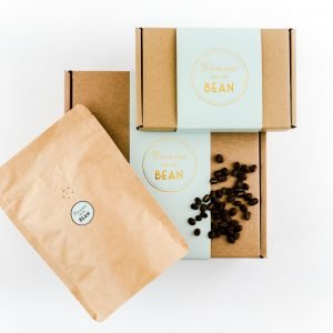 Brownie and The Bean's coffee and brownie gift set. A small branded gift box and a large packet of Butterworth & Son's coffee is balanced on top of a large branded gift box. There are loose coffee beans sprinkled on top of the large box.
