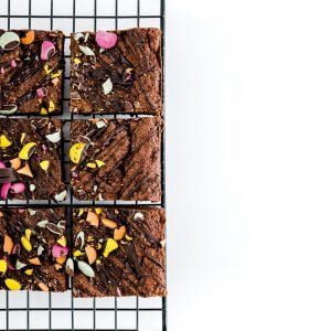 6 vegan without gluten brownies on a baking grid, on top of a white background. The brownies are cut in squares and have lots of bright coloured chocolates sprinkled all over them.