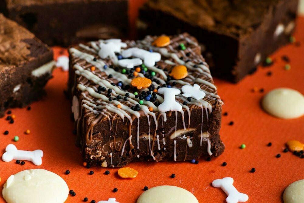 Halloween brownies on an orange background with bones, white chocolate buttons and pumpkins sprinkled on the orange background.