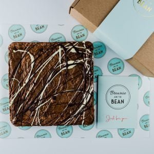 Triple Chocolate Brownie slab on branded greaseproof with a greetings card and the corner of a gift wrapped box.