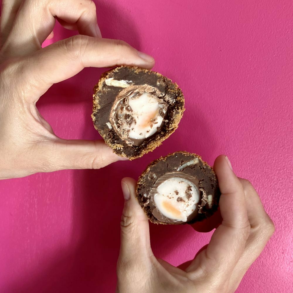 Scotch Egg Brownies being held up in two halves, against a pink background.