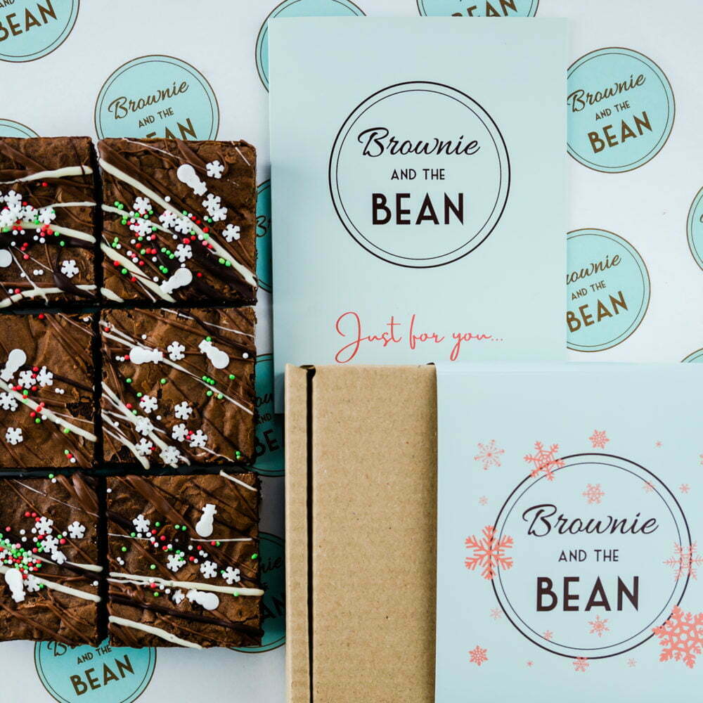 Christmas Triple Chocolate Brownie on printed greaseproof with a card and gift packaging that has snowflakes.