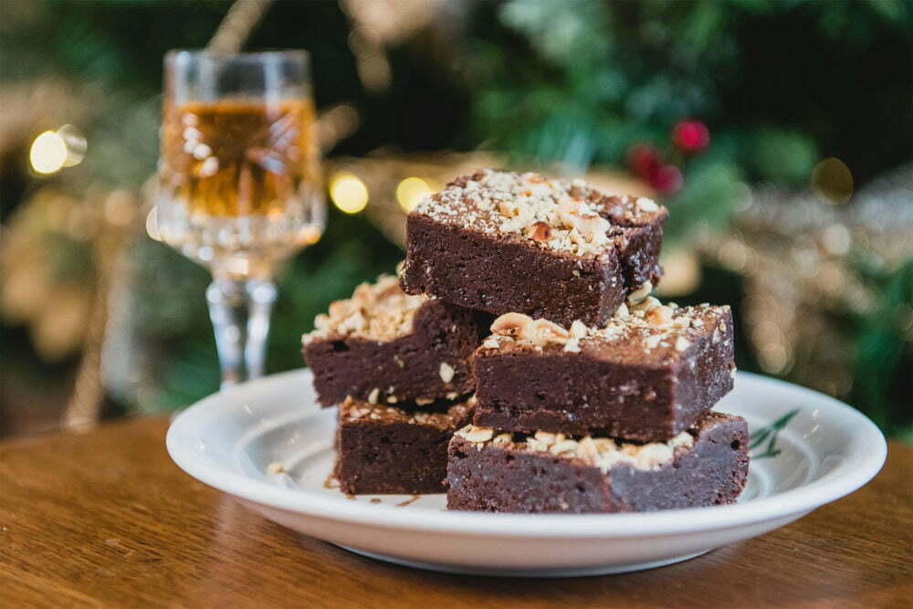 Within our small Christmas hamper you'll find the brownies featured in this image. They are The Ambassador and can be seen here on a cream plate with a Christmas tree in the background and a glass of sherry.
