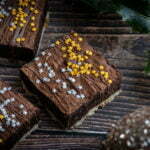 3 brownies with shortbread bases, topped with gold and silver stars are on a wooden background with holly and a glittery bauble.
