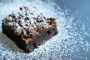 A brownie is on a blue background with icing sugar dusted all over to give the appearance of snow.