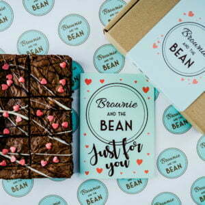 Valentine's Day Brownie Gifts on branded greaseproof. There is a card with hearts on and a brownie box with hearts on in vision.