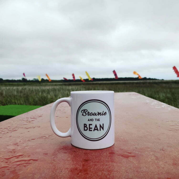 Brownie and the Bean mug on a red table with Snape Maltings in the background (at the Aldeburgh Food and Drink Festival)