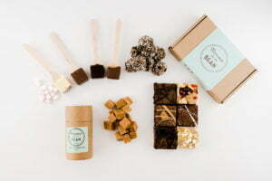 Fudge, hot chocolate stirrers, Power Balls, brownies, marshmallows and two gift boxes on a white background. One box is cylindrical with Brownie and the Bean branding, the other is rectangular with branding on too.