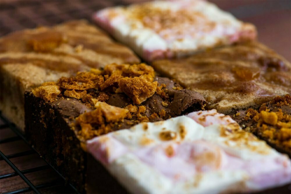6 brownies on a baking grid and dark brown background. You can see Toffee Apple Blondie, Honeycomb Brownie and S'mores Brownie.
