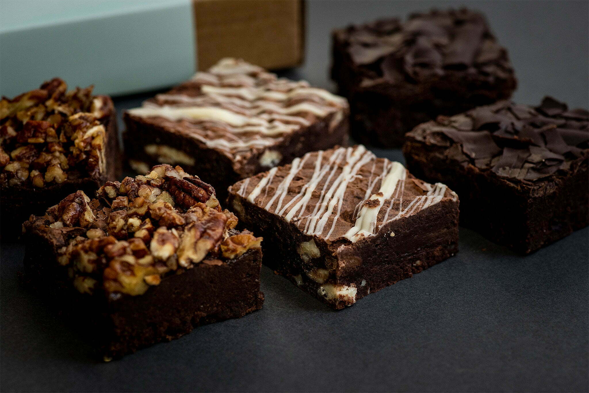 6 brownies laid out on a dark background with a brownie box in the background.