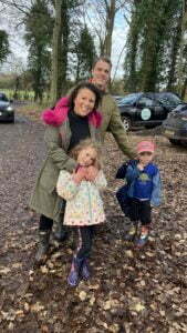 Charlotte and Luke are photographed with their children in a forest. They are happy.
