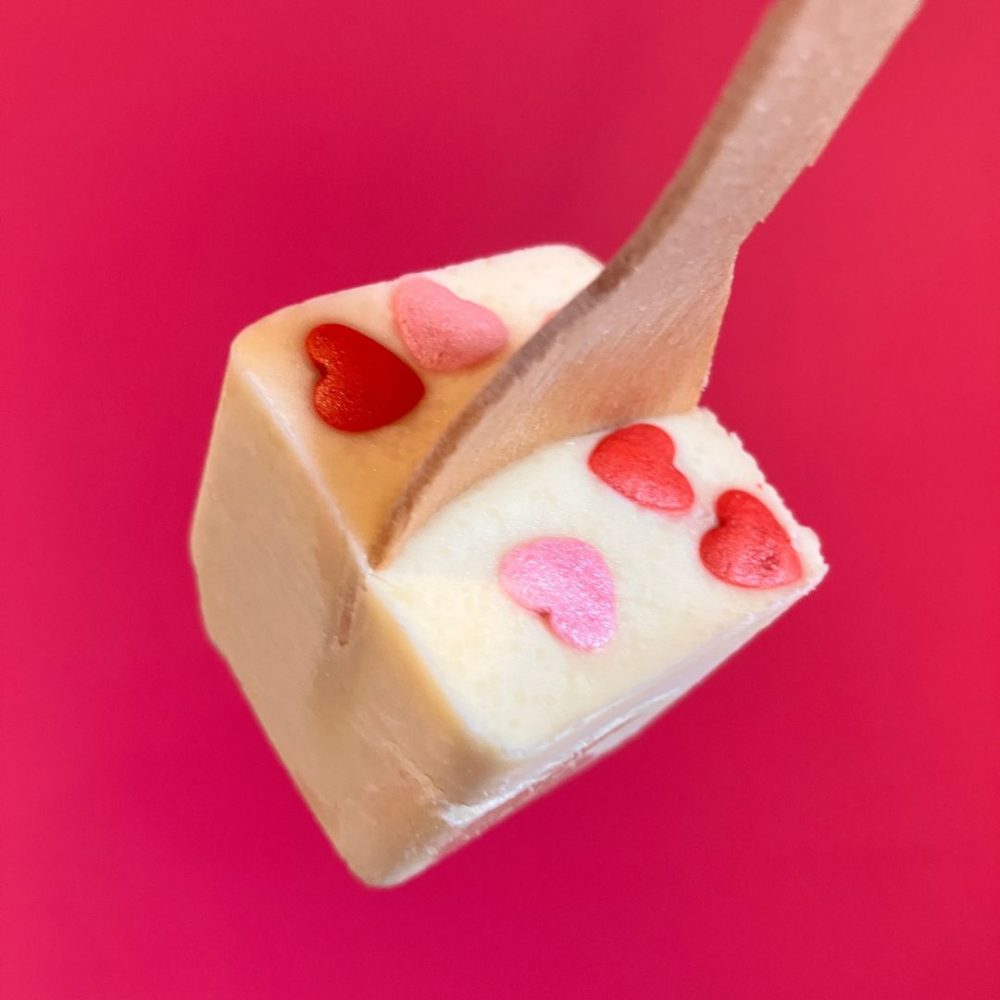 Mother's Day and Valentine's Day hot chocolate stirrer on a pink background. Hot chocolate stirrer is made with white chocolate and there are pink and red hearts set into it.
