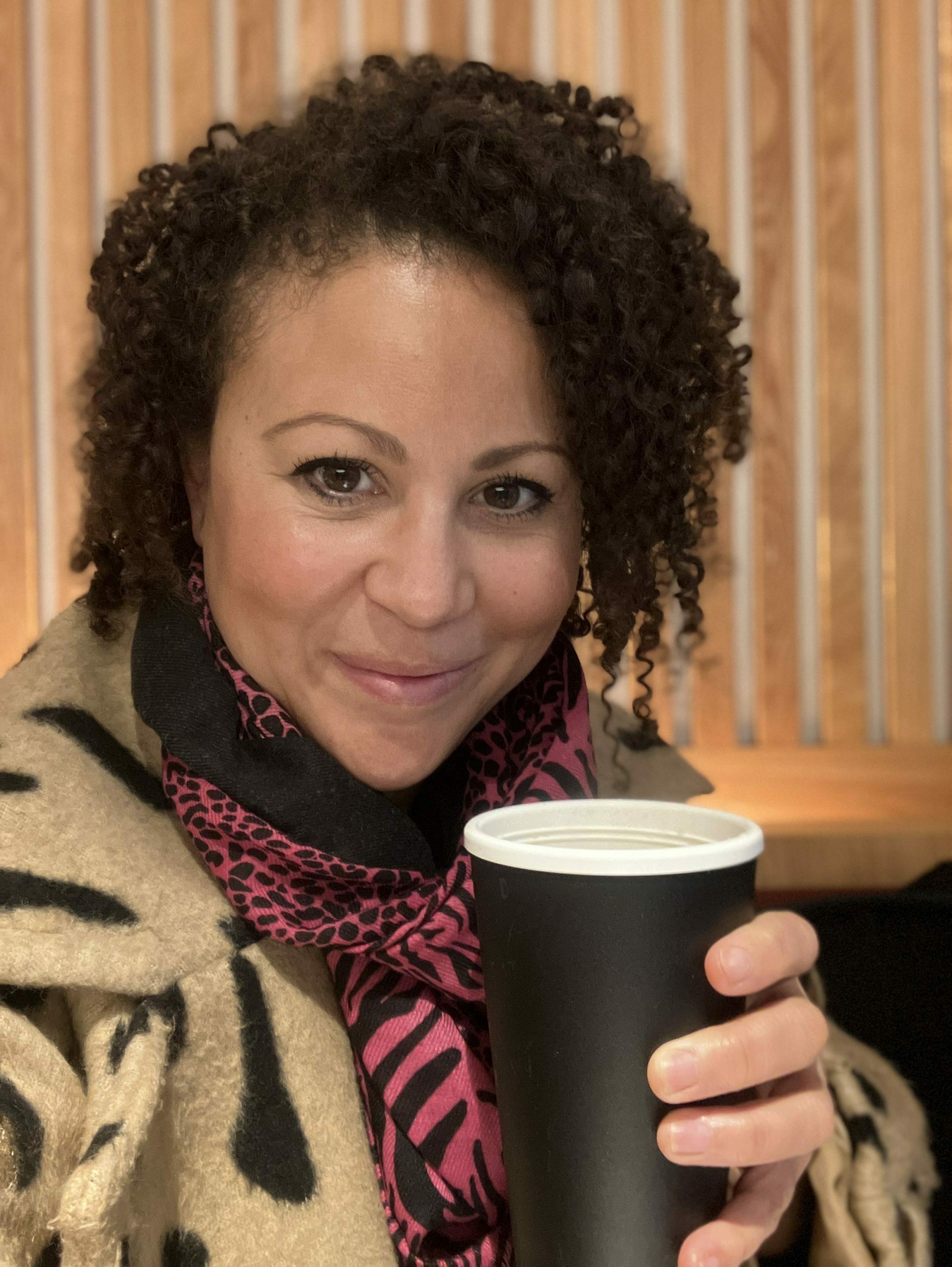 Charlotte from Brownie and the Bean smiling and holding a reusable cup. She was waiting in London to enter the Rose Review progress report event.