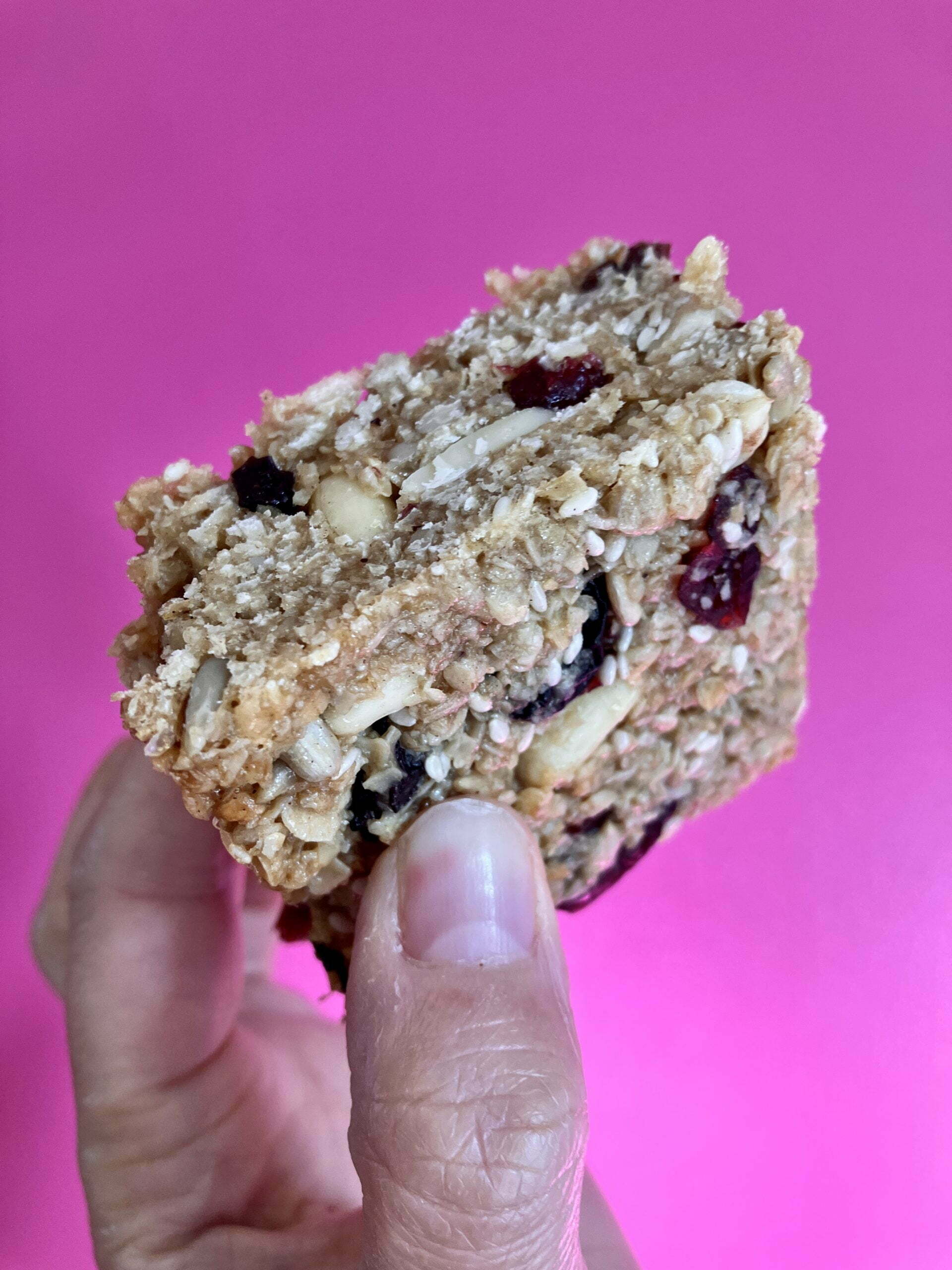 A granola bar is shown held up against a pink backdrop. The granola bar is part of our wholesale bakery offering.