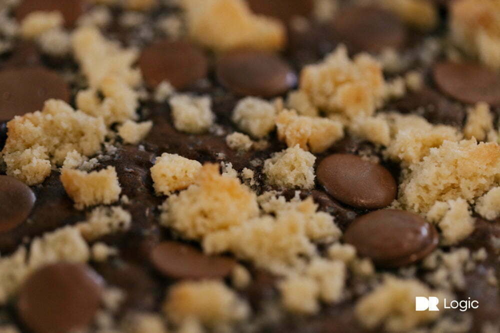 A close up of a chocolate billionaire brownie slab with chocolate buttons and shortbread crumbled on top