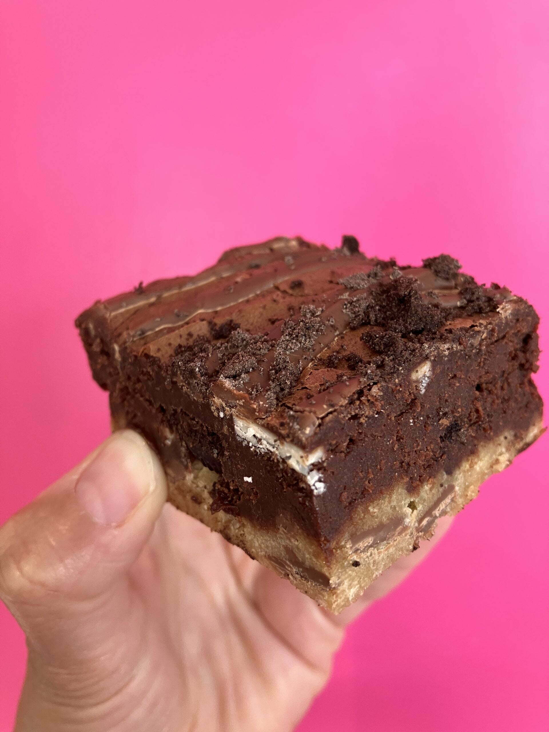 Someone is holding a brownie for wholesale against a pink background