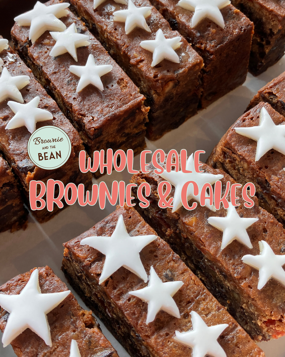 Wholesale cakes are lined up diagonal across the photo. The cakes have starred icing toppings and the text reads "Wholesale Brownies & Cakes". The Brownie and the Bean logo is to the left of the text. The cakes are brown fruit cakes with raisins.
