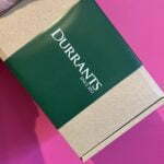 Brownie box with a green sleeve branded by Durrants is held up against a pink background.