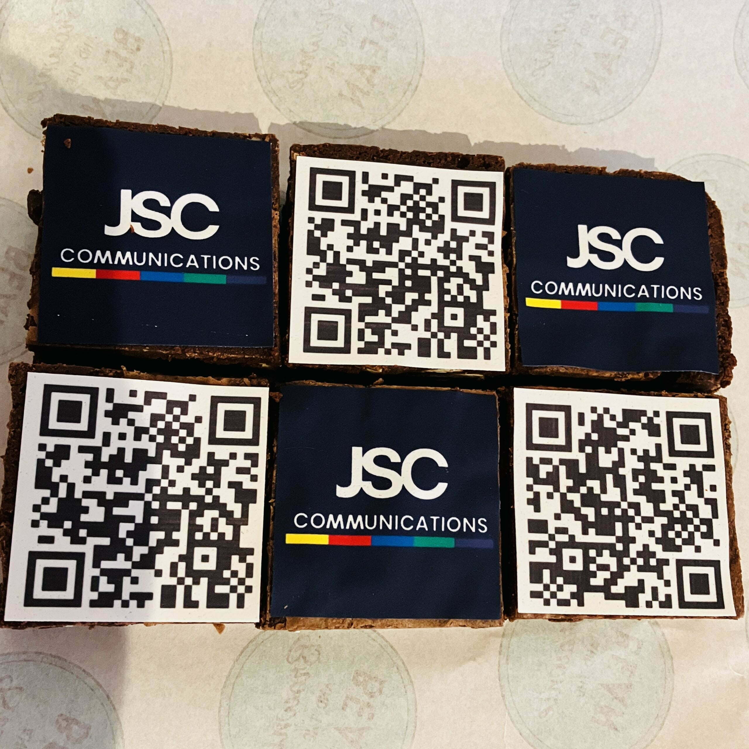 our Corporate Gifting Brownies are laid on a sheet of greaseproof paper. Three chocolate brownies have a business company logo on them, three of the chocolate brownies have a QR code on them, which links the recipient to a showreel of the business sending them brownies.