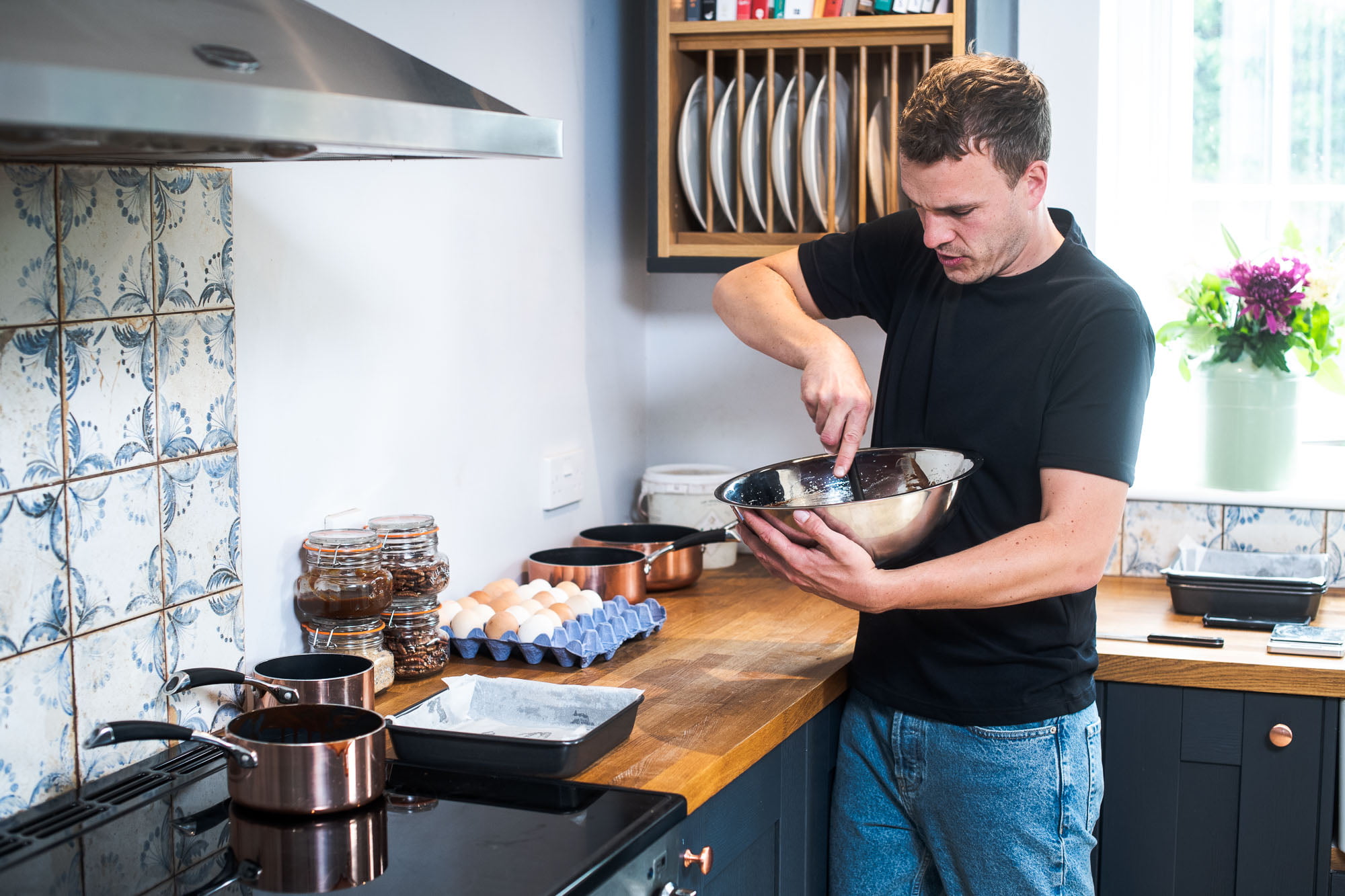 Luke (Brownie and the Bean co-founder) has a mixing bowl in his hands. Inside the mixing bowl is chocolate. He is in a modern style family kitchen with eggs and various other ingredients on the counter.