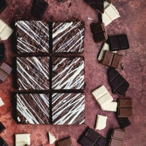 6 of our Triple Chocolate Brownies are on a brown marbled background. There are milk, dark and white chocolates squares surrounding the 6 brownies.