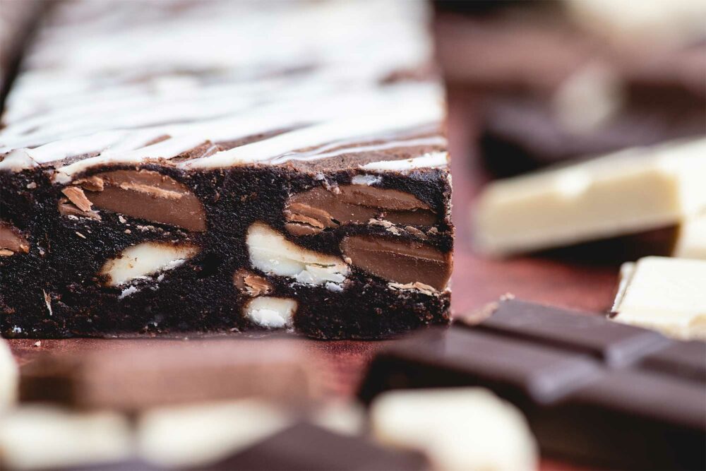 A profile of a triple chocolate brownie is surrounded by milk, dark and white chocolate squares surrounding the brownie.