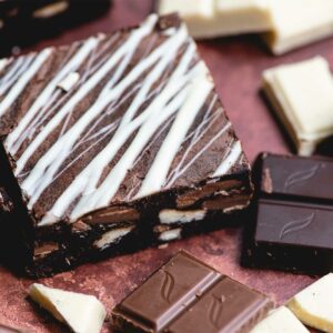 A triple chocolate brownie is surrounded by another 2 brownies. There are also milk, dark and white chocolate squares surrounding the brownie.
