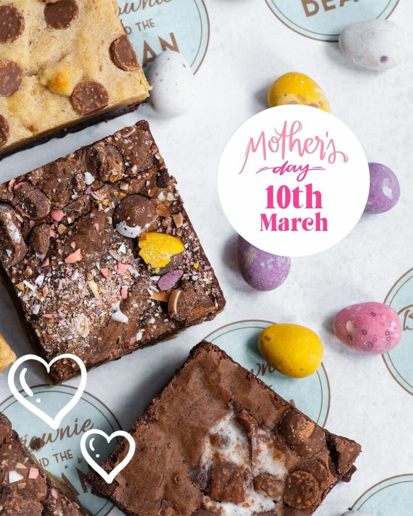 Image says "Mother's Day 10th March". In the background is Brownie and the Bean branded greaseproof paper and there are 2 brownies and one cookie dough brownie in the image. There are also Mini Eggs in pastel shades to the right of the picture and hearts to the left of the screen